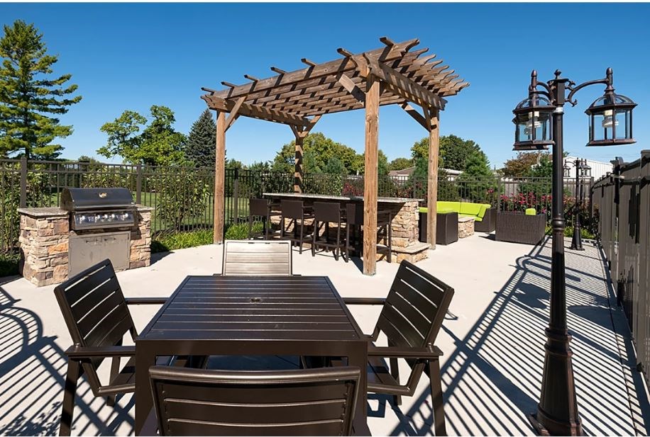 A wooden table is surrounded by chairs under a pergola on a patio.