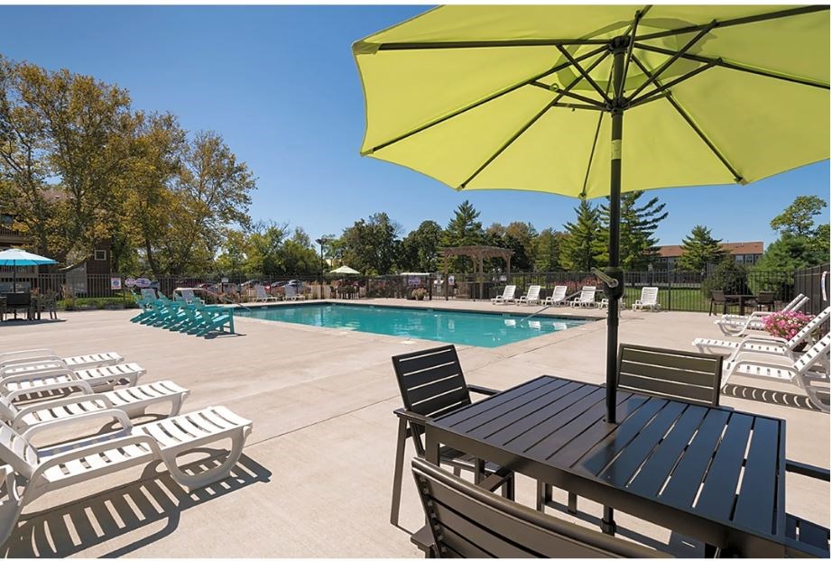 A yellow umbrella is in the foreground of a pool area with sun loungers.