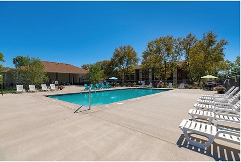 A pool surrounded by chairs and trees.