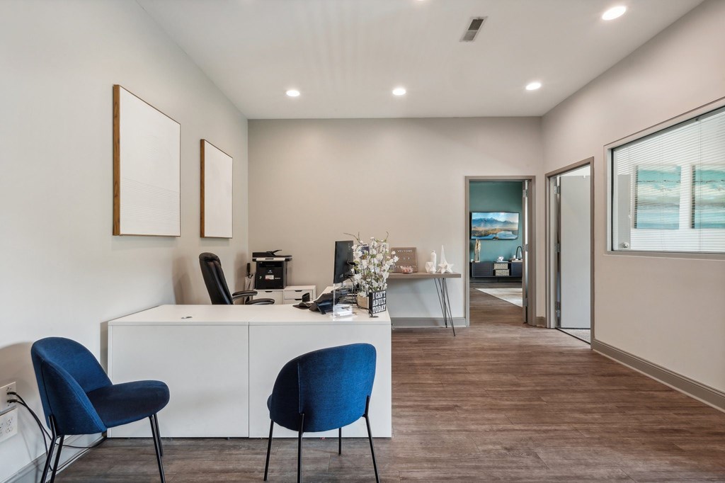 A room with a desk, chairs and pictures on the wall.