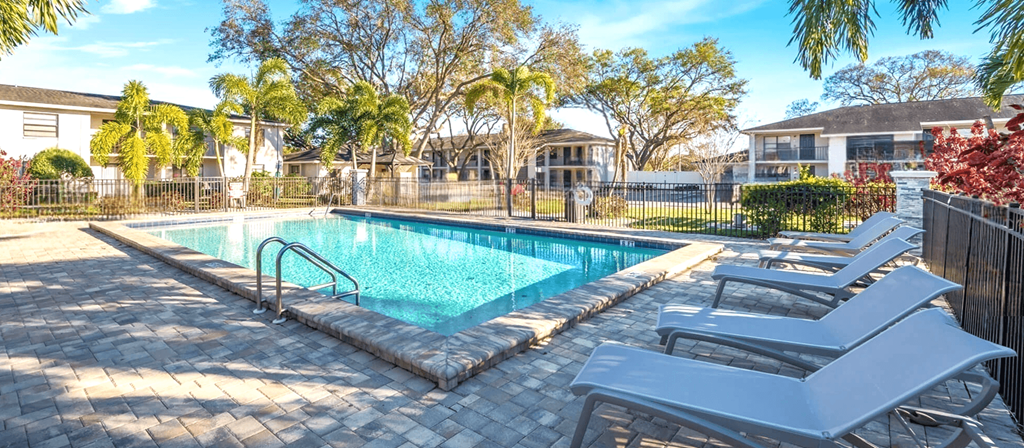 A pool surrounded by lounge chairs and trees.