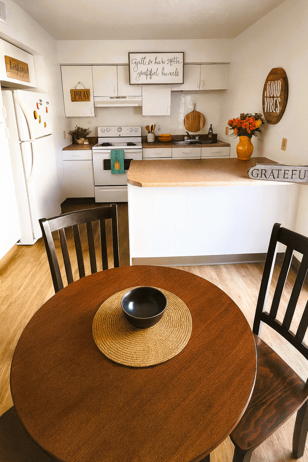 A kitchen with a table and chairs in the foreground and a fridge with magnets on it in the background.