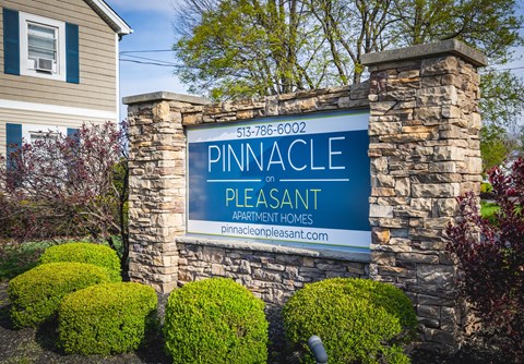 A sign for Pinnacle Pleasant Apartment Homes is displayed in front of a house.