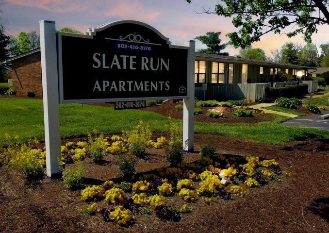 a sign for state run apartments in front of a garden