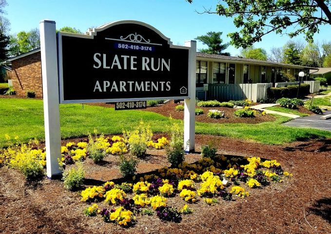 a sign for state run apartments in front of a garden of flowers