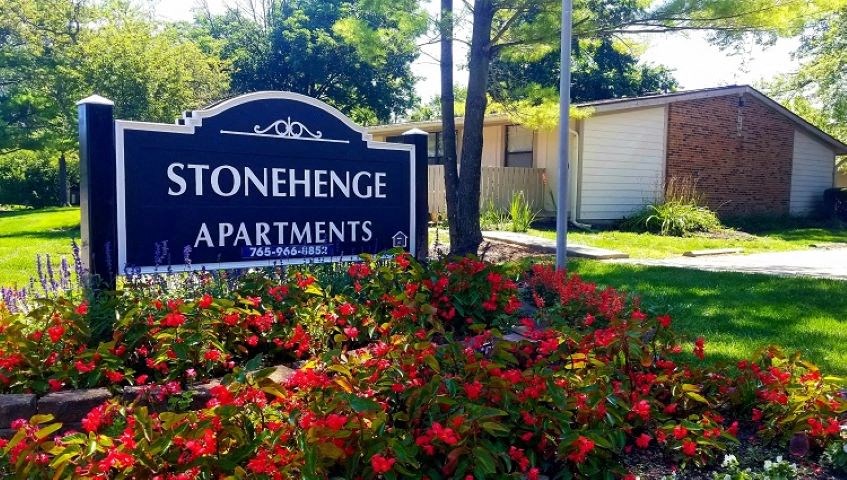 a sign for stonehenge apartments in front of red flowers