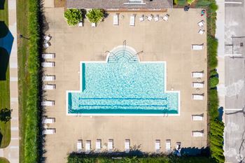 An aerial view of a pool surrounded by a concrete deck and lounge chairs.