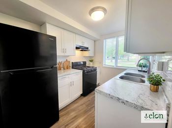 A kitchen with a black fridge, white cabinets, and a marble countertop at Townhomes at 28th, Indiana, 47201