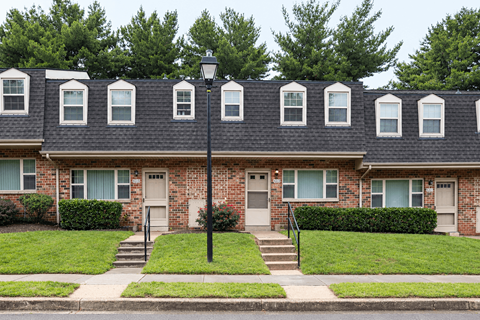 A row of houses with green bushes in front at The Orchards at Severn Townhomes*, Severn, MD 21144.