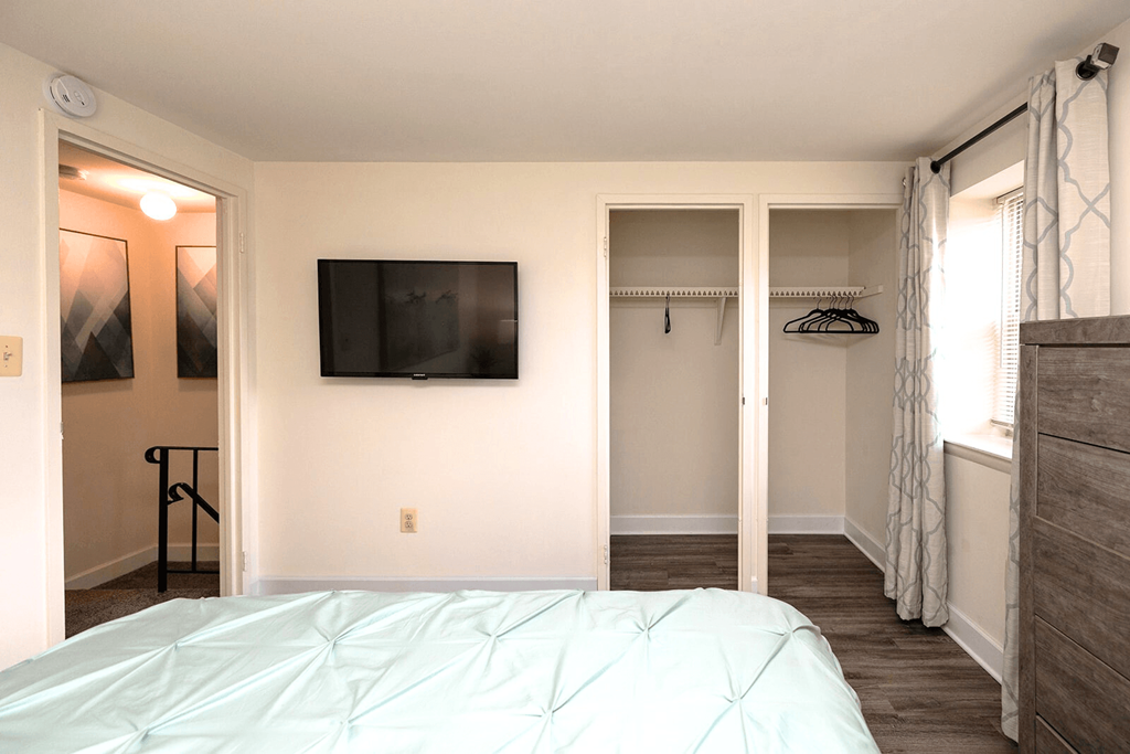 A bedroom with a bed, a TV, and a window with curtains.