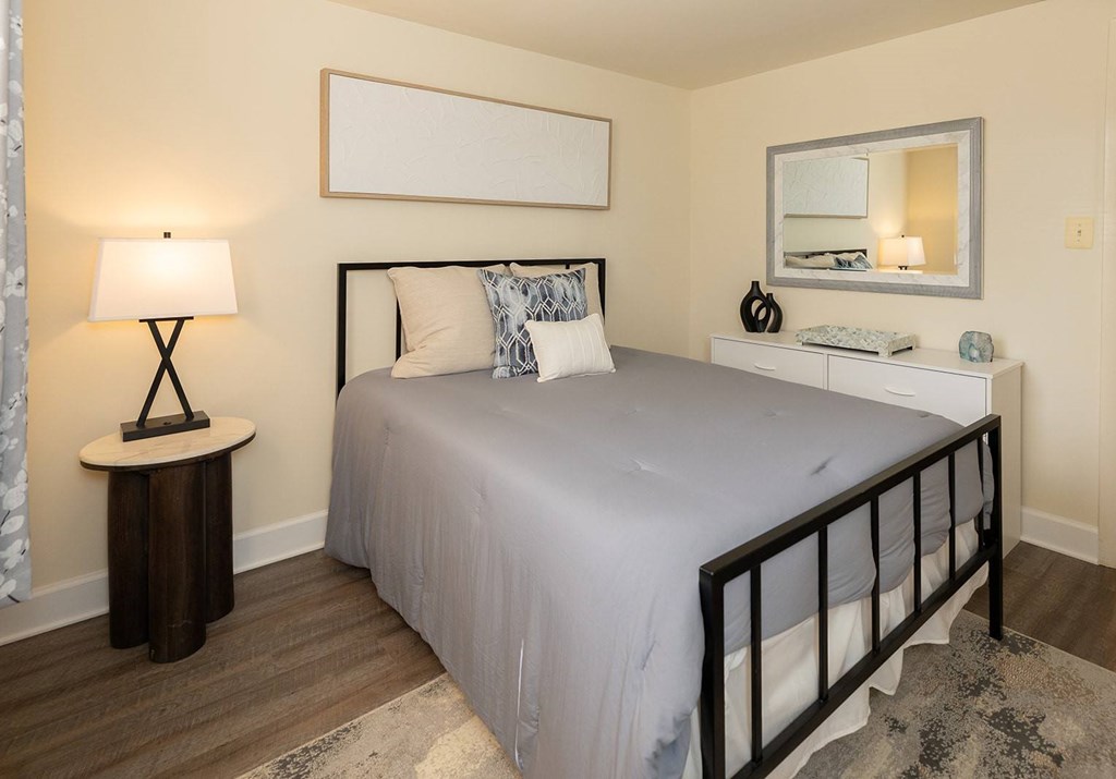 A bedroom with a bed, nightstand, and lamp at Hyde Park Apartments*, Essex, MD 21221