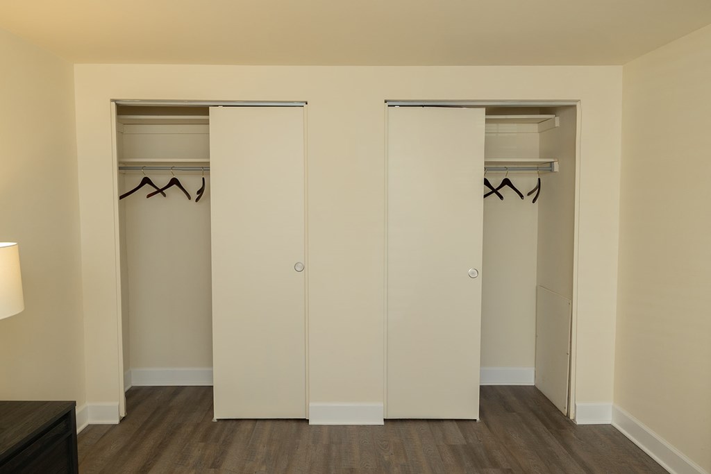 Two white closet doors with clothes hanging on them at Hyde Park Apartments*, Essex, MD 21221