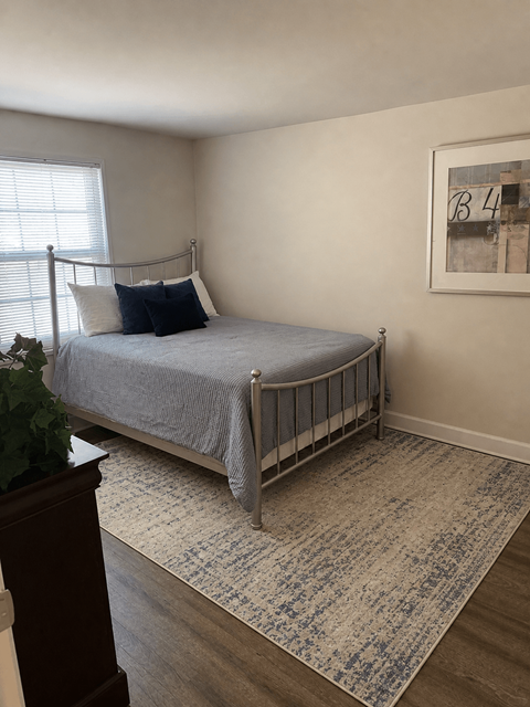 A bedroom with a bed, a rug, and a painting on the wall.