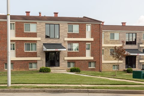 A red brick apartment building with a green lawn in front at Winston Apartments, Baltimore, Maryland