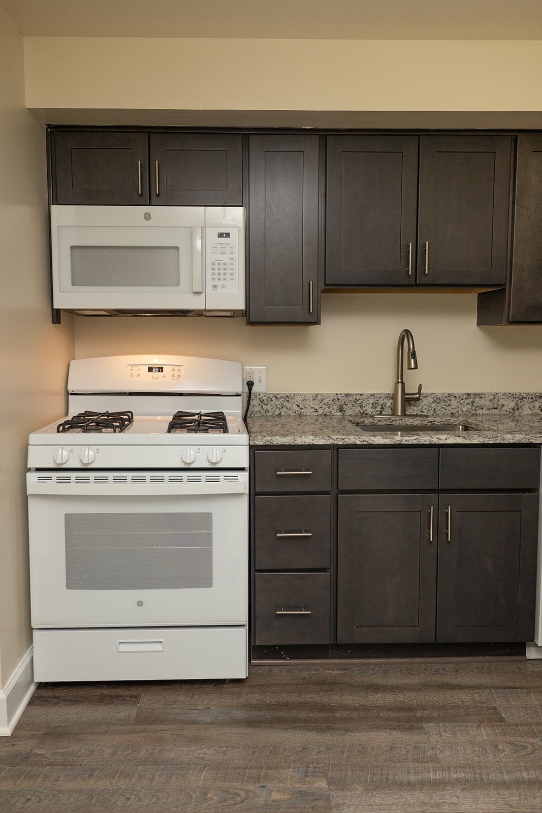 A white stove and microwave in a kitchen with dark brown cabinets.
