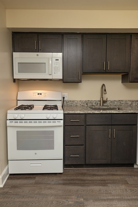 A white stove and microwave in a kitchen with dark brown cabinets at The Orchards at Severn Townhomes*, Severn, MD 21144