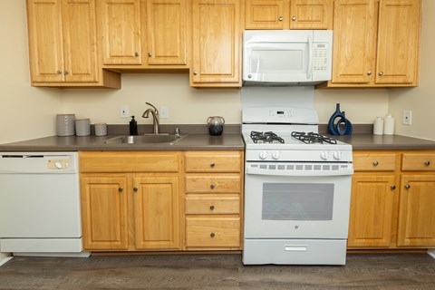 A kitchen with wooden cabinets and a white stove top oven. at Colony Hill Apartments & Townhomes, Baltimore, MD