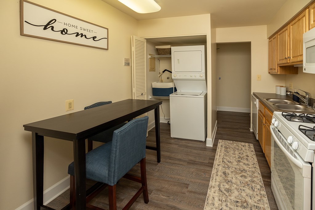 A kitchen with a table and chairs in front of a sign that says Home Sweet Home at The Brittany Apartments, Maryland