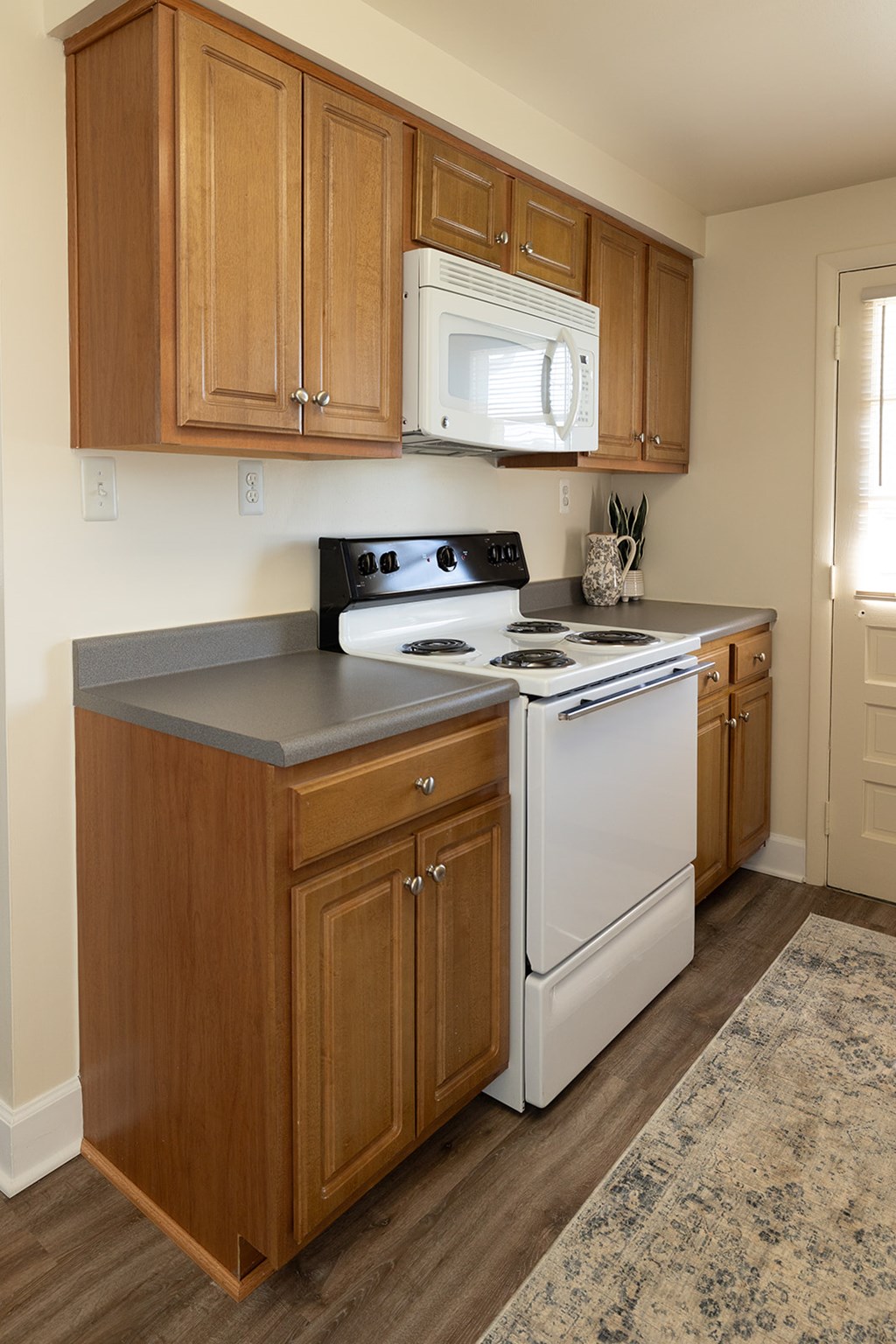 Wooden kitchen cabinets with white microwave and oven with gas range at Walnut Grove Townhomes*, Maryland