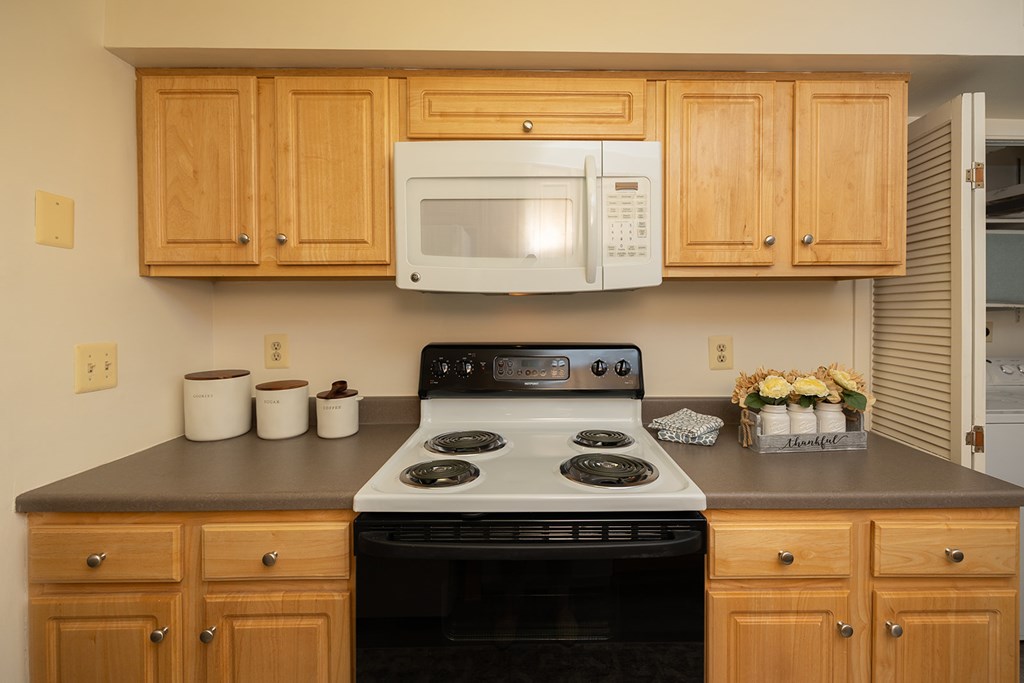 A kitchen with a white microwave above a stove and wooden cabinets.at Chapel Valley Townhomes, Maryland, 21236