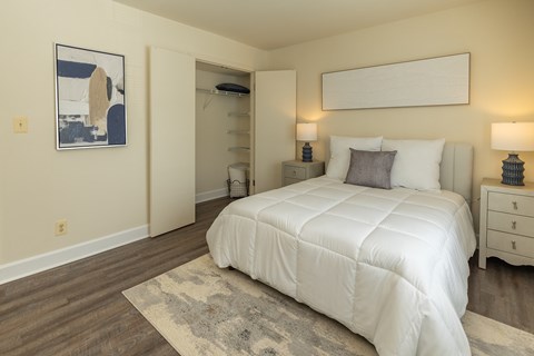 A bedroom with a large bed, two nightstands, and a rug at The Brittany Apartments, Pikesville, Maryland