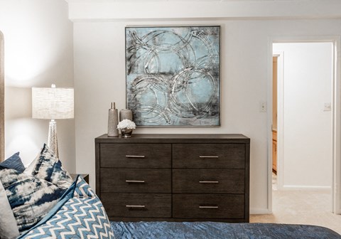 A bedroom with a bed, a dresser, and a painting on the wall.
