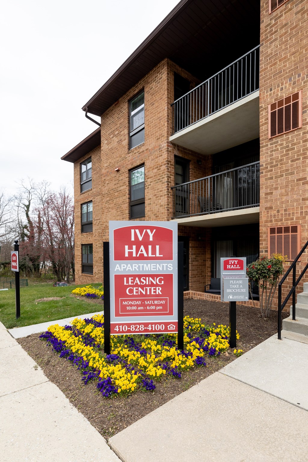 A sign for Ivy Hall Apartments leasing center in front of a brick building.