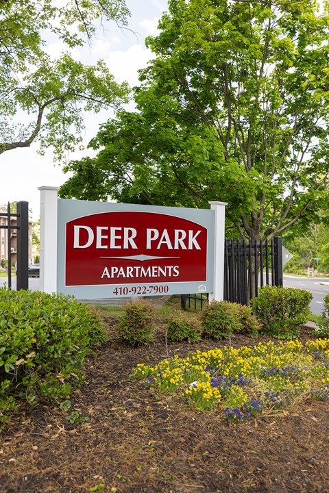 A sign for Deer Park Apartments is in front of a fence and trees.