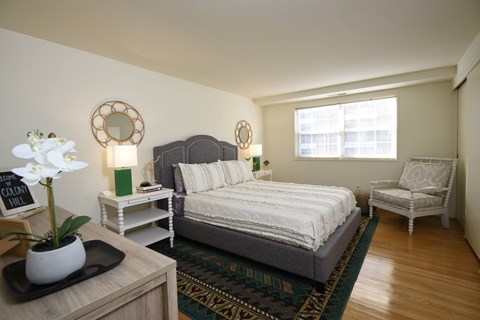 A bedroom with a bed, chair, and a flower vase on a table.