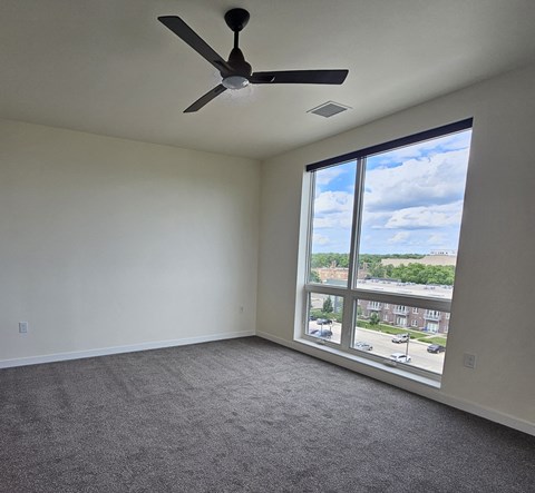 an empty living room with a large window and a ceiling fan