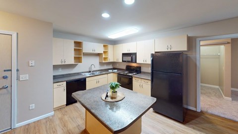 A kitchen with a black refrigerator and a table with a vase of flowers on it.