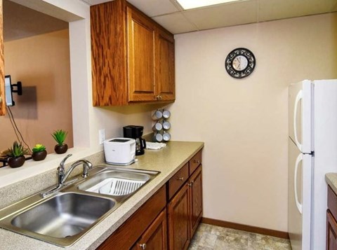 A kitchen with a white fridge, wooden cabinets, and a clock on the wall.