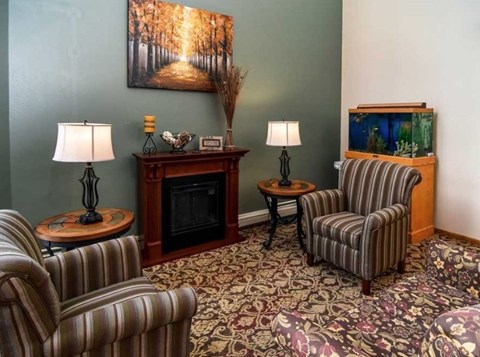 A living room with a fireplace, two striped chairs, and a fish tank.