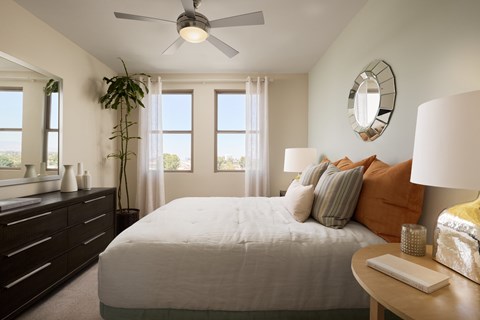A bedroom with a bed, a dresser, a ceiling fan, and a window with curtains.