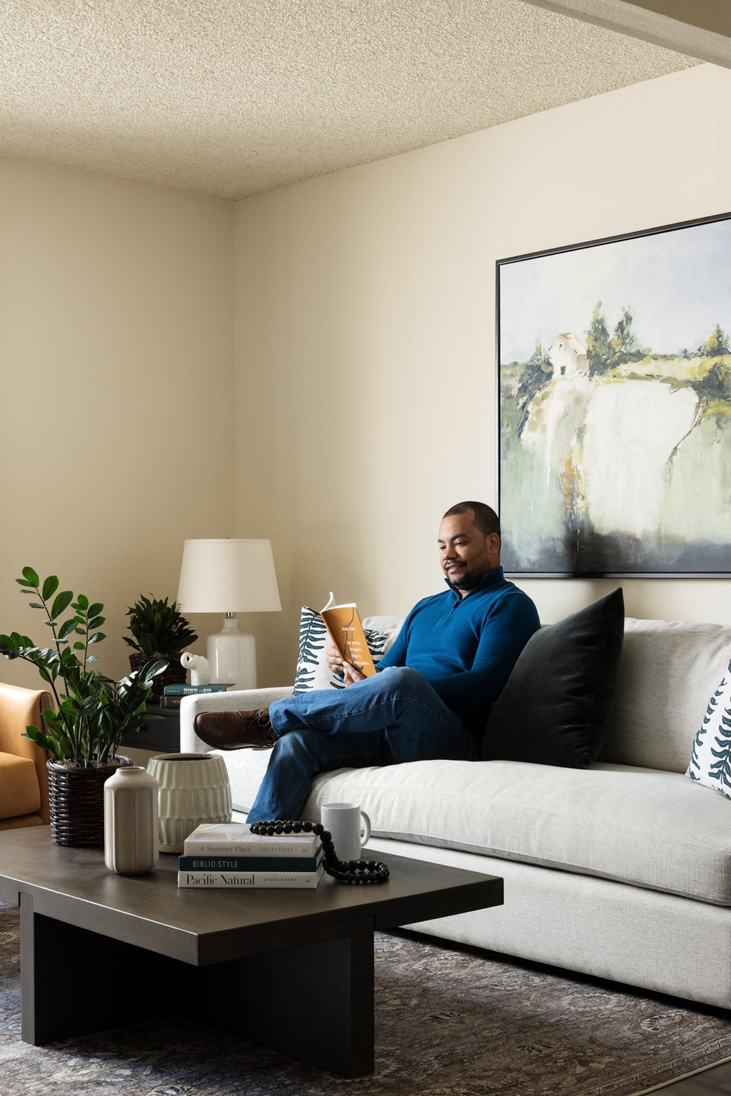 Man reading book on couch in living area at Cerritos Apartments