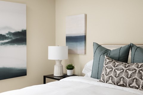 A bed with a side table and wall art at Crystal Springs apartments in Fountain Valley.