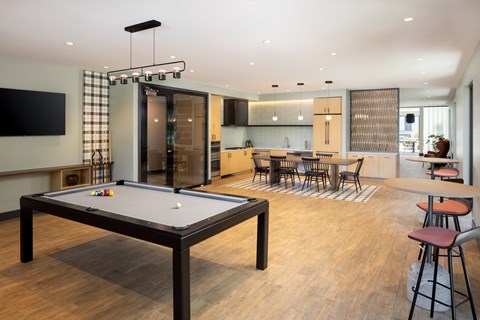 A billiard table is in the middle of a room with a kitchen in the background.