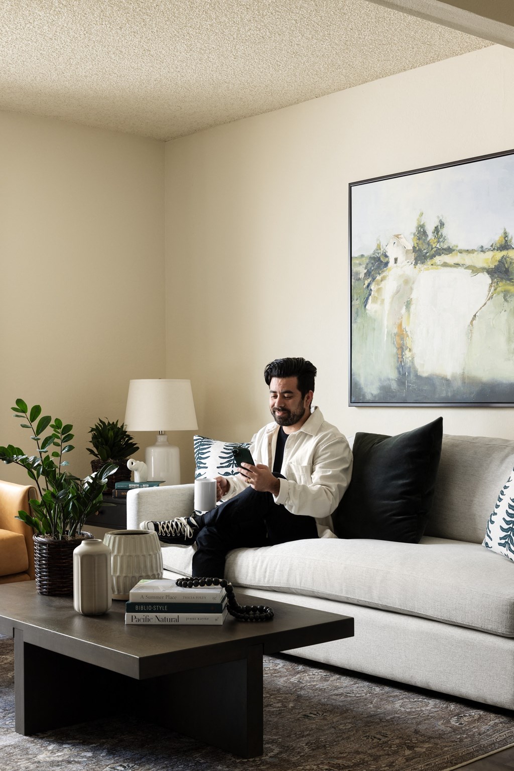 Man drinking coffee and looking at phone in living space at Cerritos Apartments