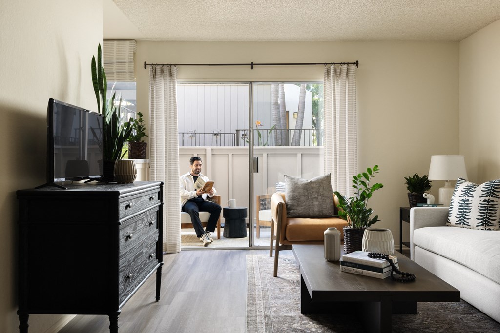 Man with facial hair reading book in patio space at Cerritos Apartments