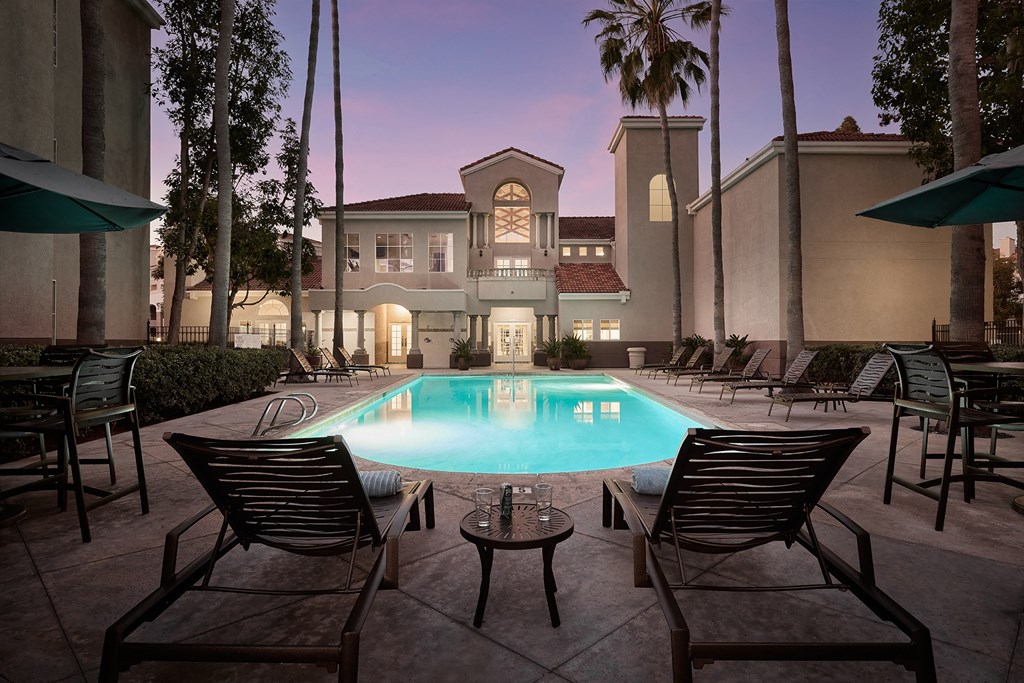 A pool surrounded by chairs and tables in front of a house  Valentia Apartments in La Jolla.