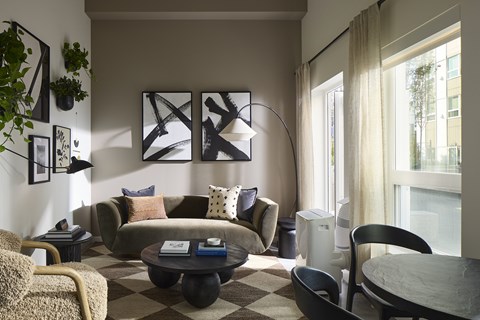 A living room with a grey couch situated near a large window overlooking the courtyard at Verdant Apartments in Shoreline.