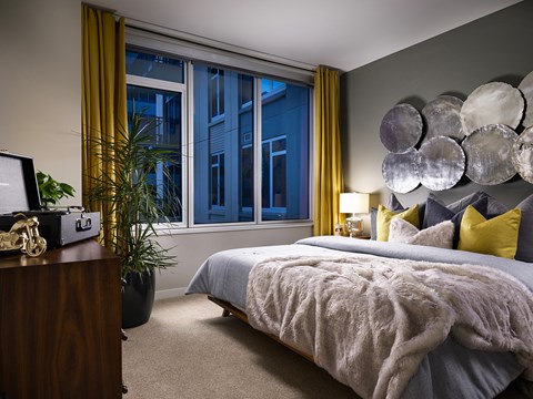 A model bedroom with a large window, a queen sized bed, and a vanity at The Quincy in Downtown Denver.