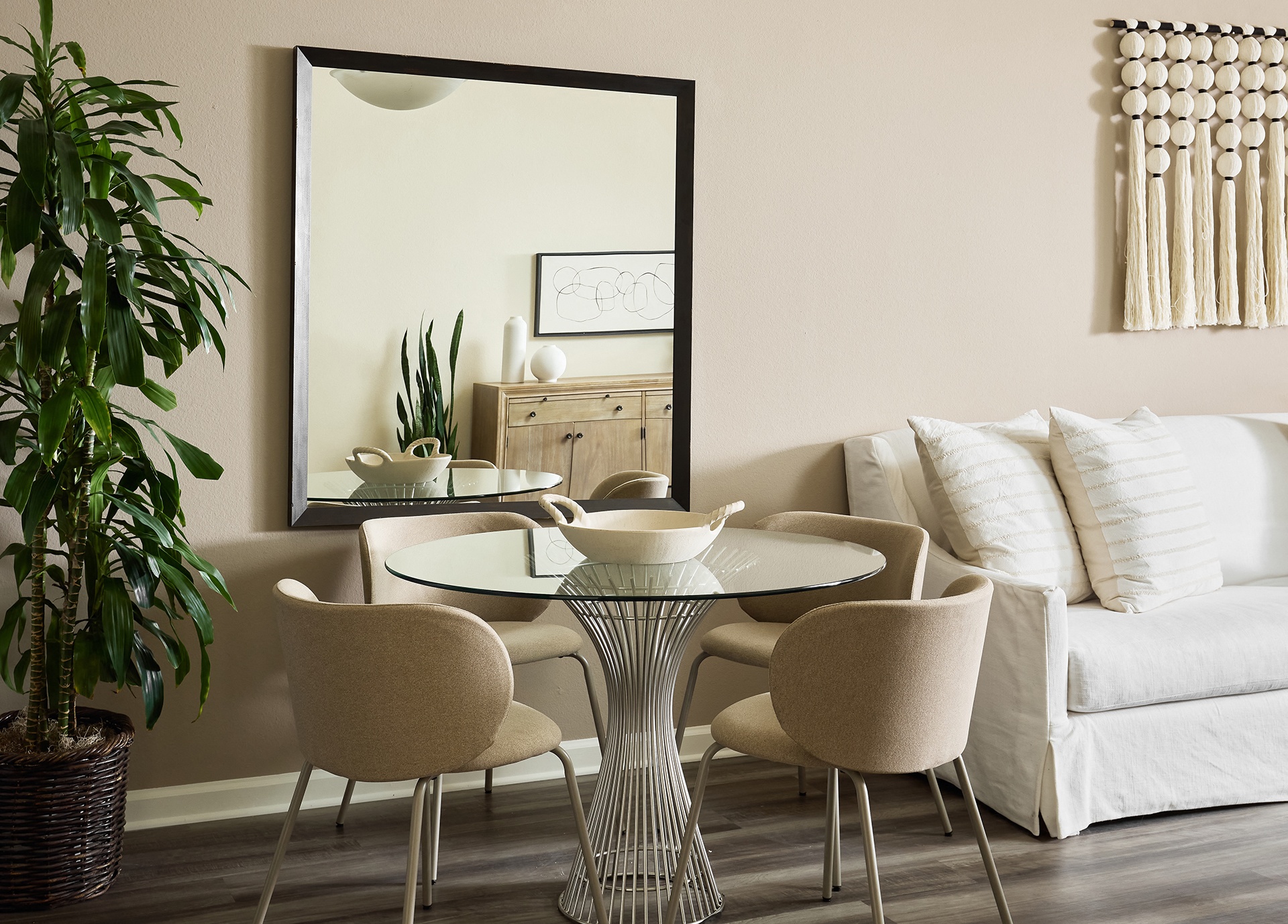A living room with a glass table and chairs, a potted plant, and a white couch at Valentia Apartments in La Jolla at Valentia Apartments in La Jolla.