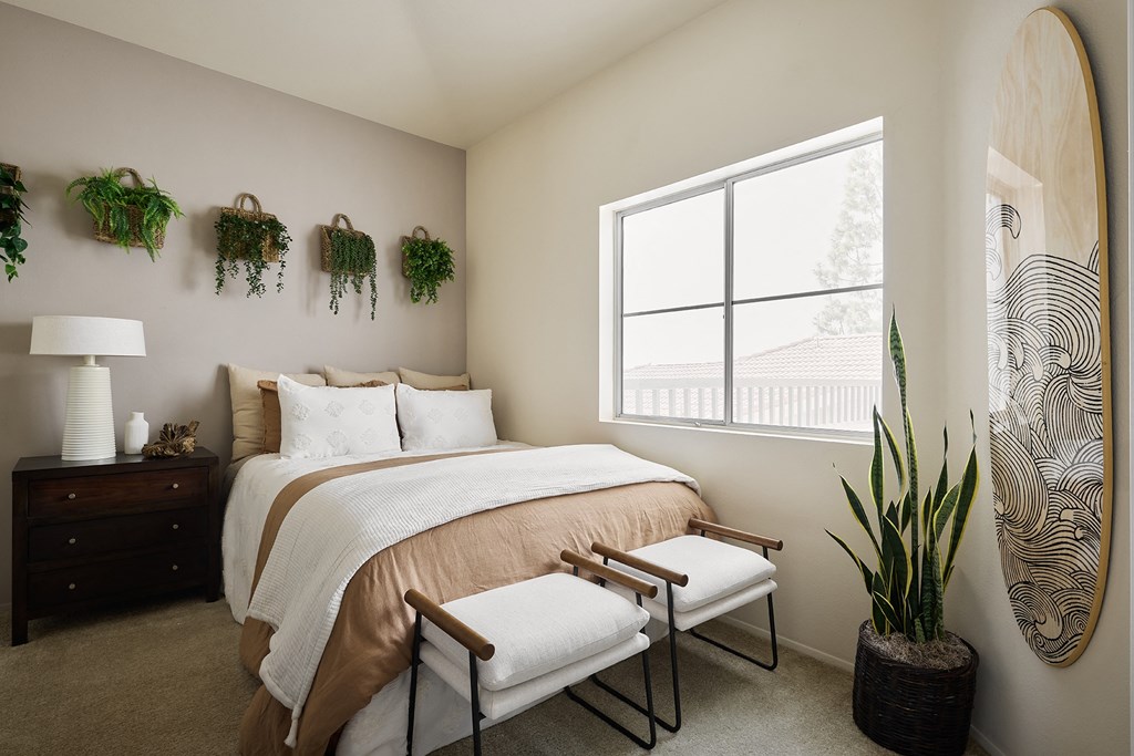 A bedroom with a bed, chair, and a surfboard leaning against the wall at Valentia Apartments in La Jolla at Valentia Apartments in La Jolla.