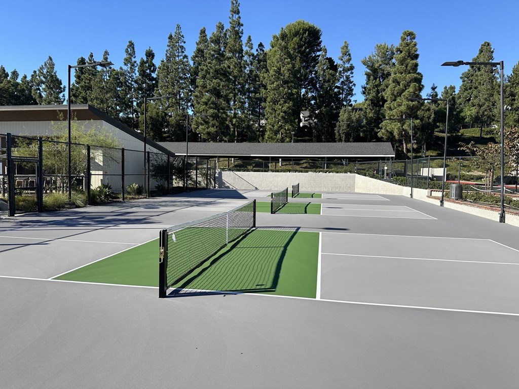 Tennis court with four tennis courts and a building in the background at Seaside at Laguna Heights apartments in Laguna Niguel.