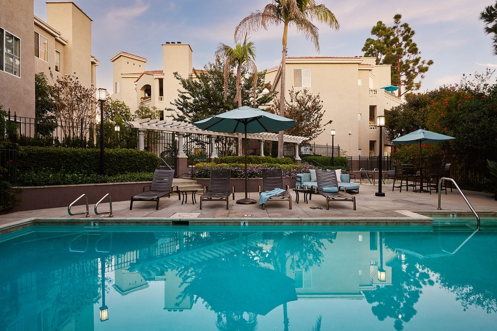 A pool with a blue umbrella and chairs in front of a building at Valentia Apartments in La Jolla.