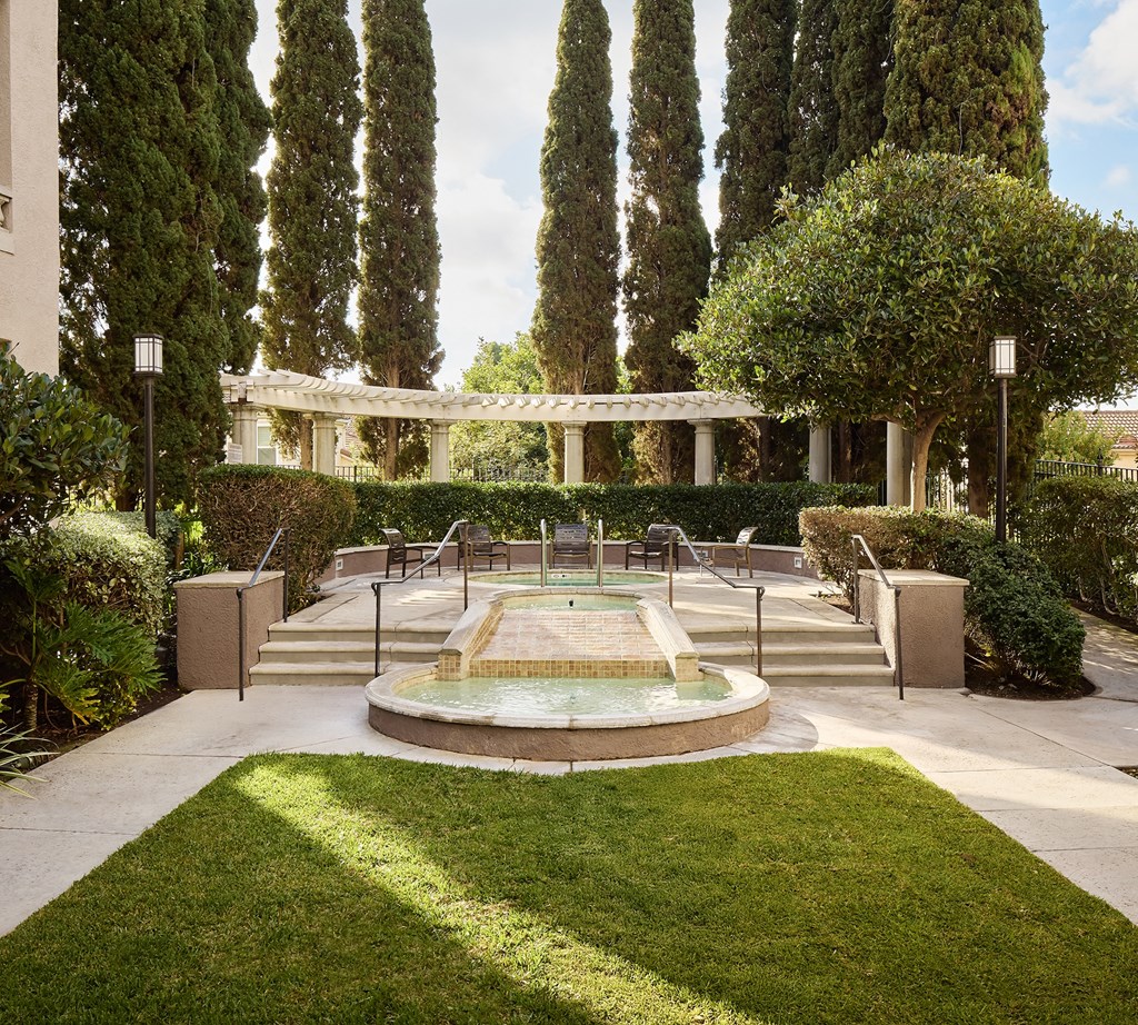 A fountain in the middle of a grassy area surrounded by trees at Valentia Apartments in La Jolla.
