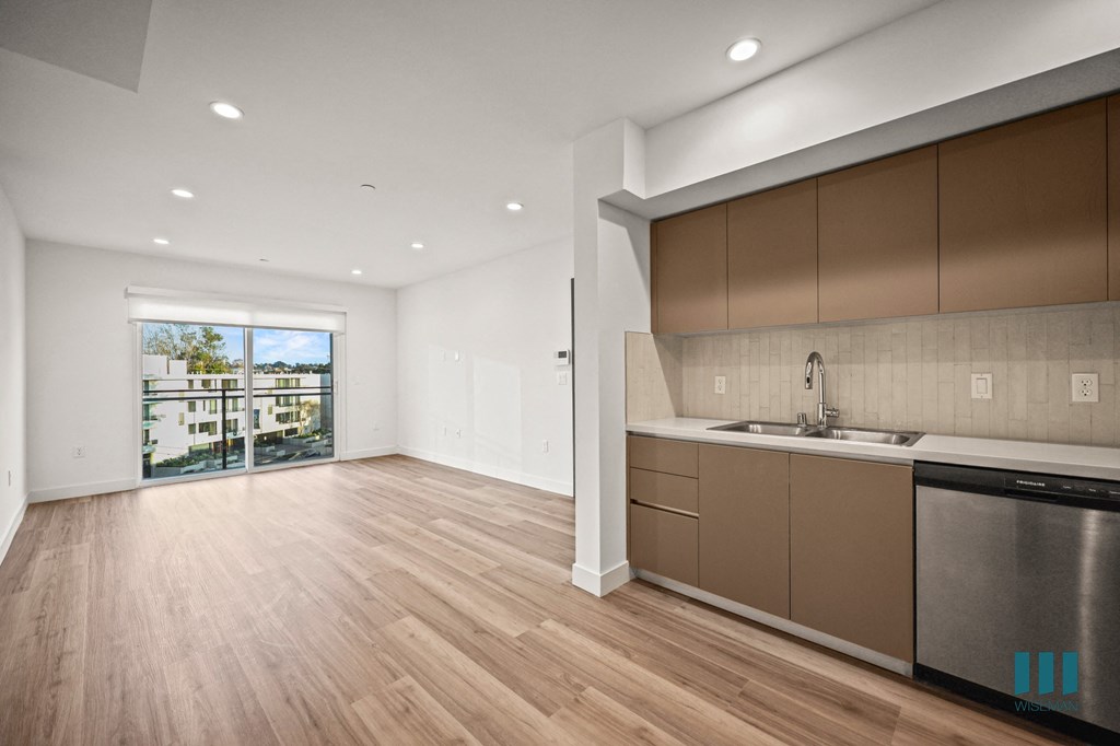 A kitchen with a stainless steel dishwasher and wooden flooring.
