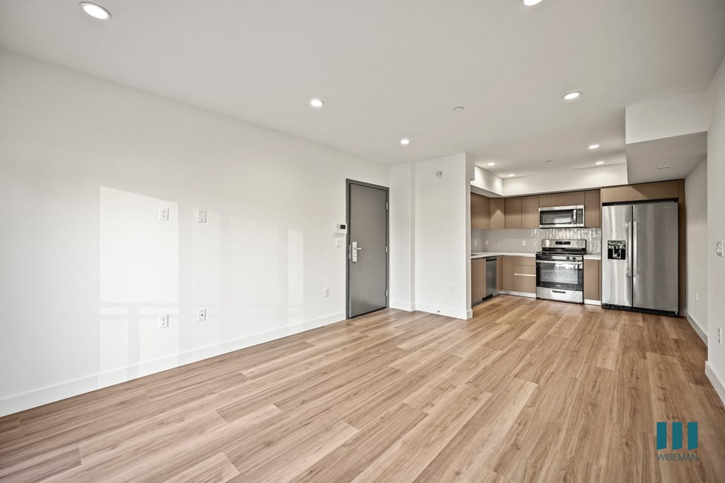 A kitchen with a white wall and wooden floors.