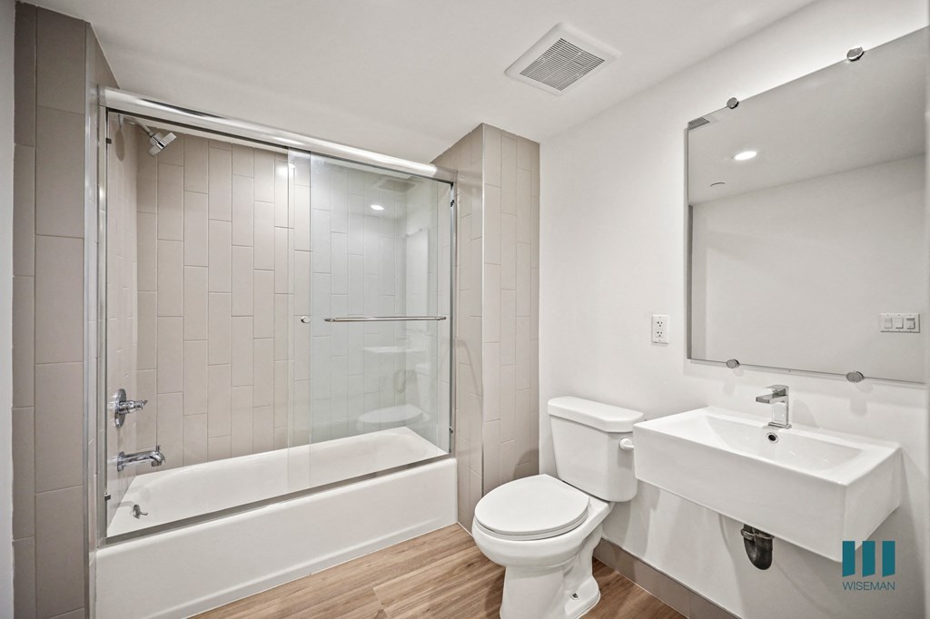 A white bathroom with a toilet, sink, and a glass shower stall.